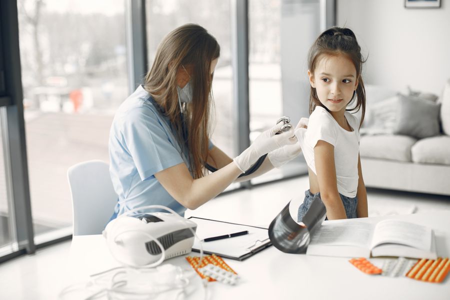 A pediatrician examining a smiling girl in a bright clinic
